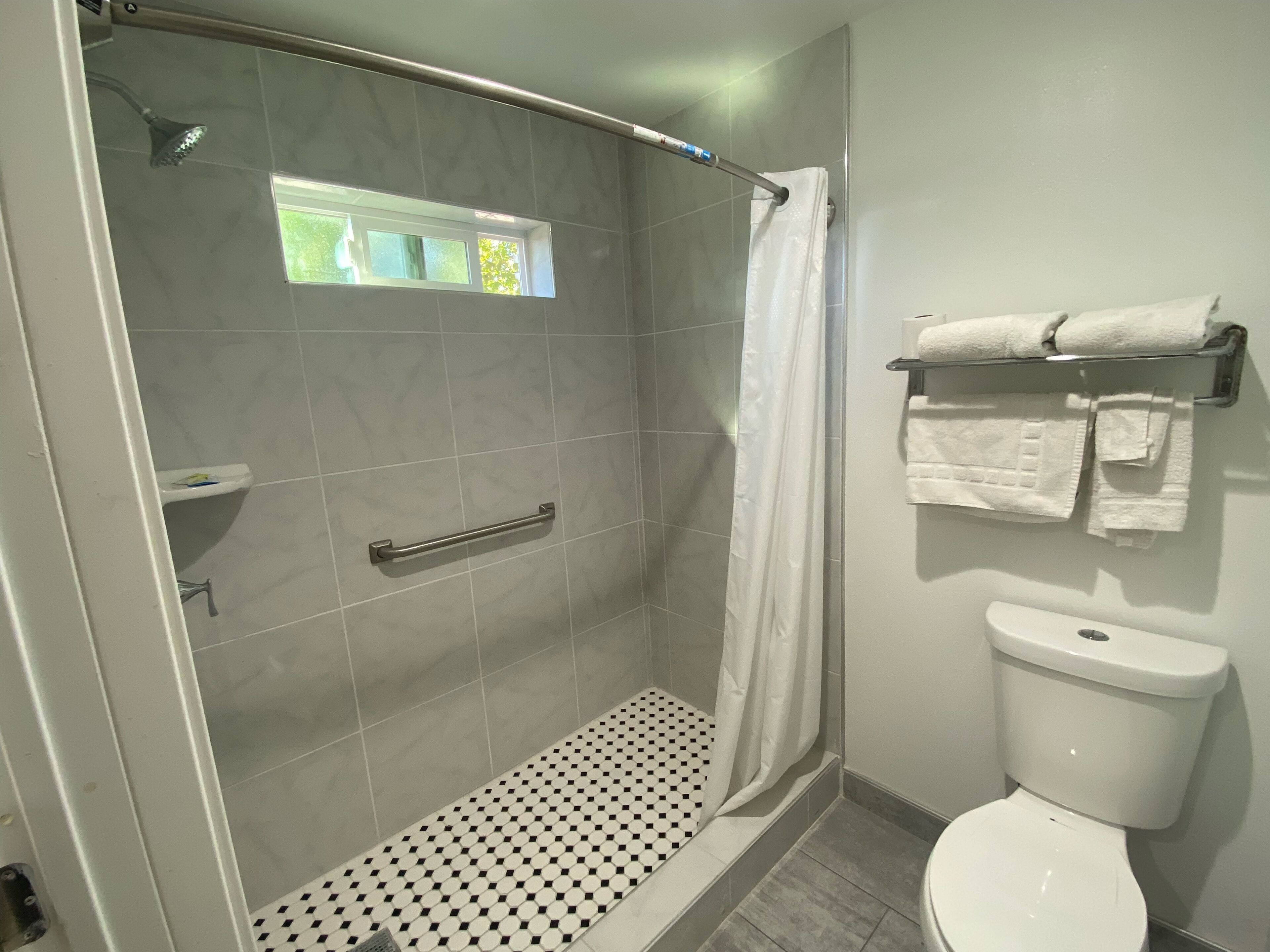 Un baño moderno con ducha, inodoro y un pequeño ventanal.