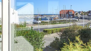 Uma marina com barcos atracados, uma estrada em primeiro plano e edifícios ao fundo.