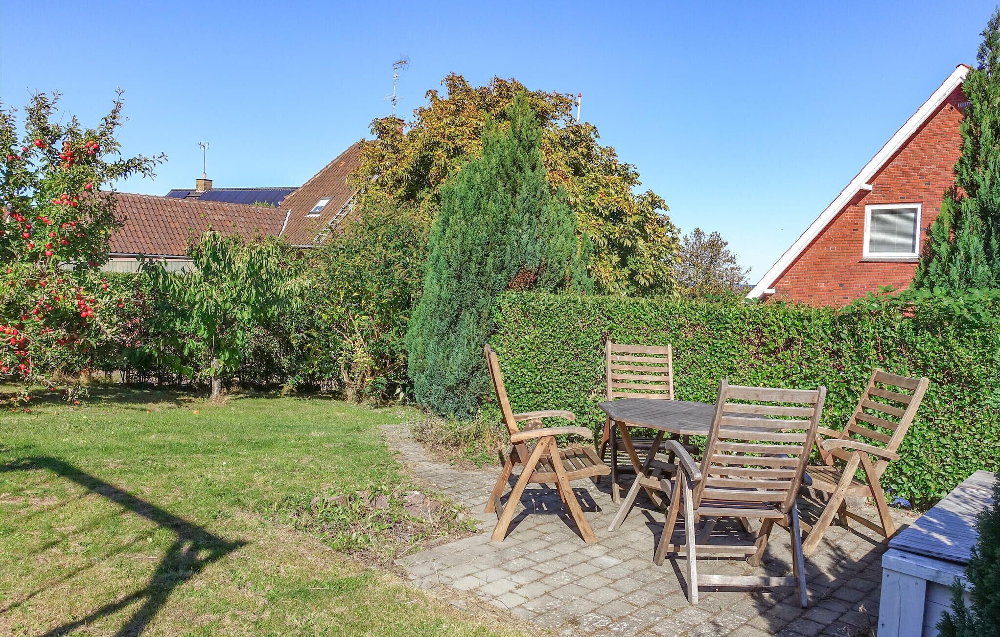 Een terras met een tafel en vier houten stoelen, omgeven door een haag en een gazon.