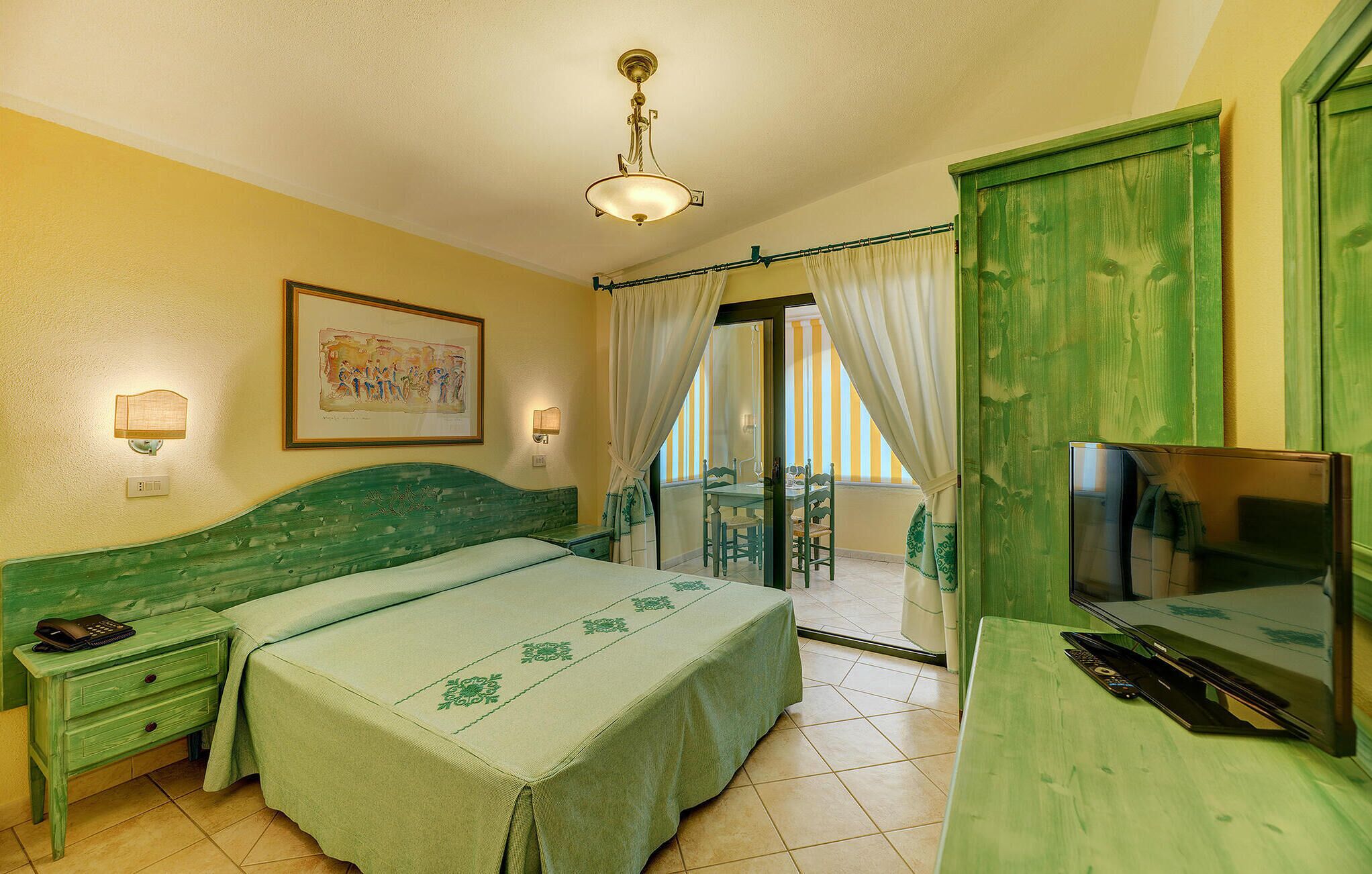 A room with a bed, a desk with a TV, a chair, a table, and a window with curtains.