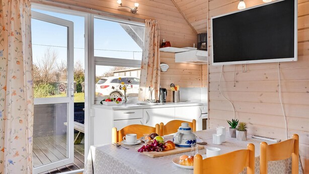 Una cocina acogedora con comedor, que cuenta con un amplio ventanal, un televisor de pantalla plana y una mesa lista para el desayuno.