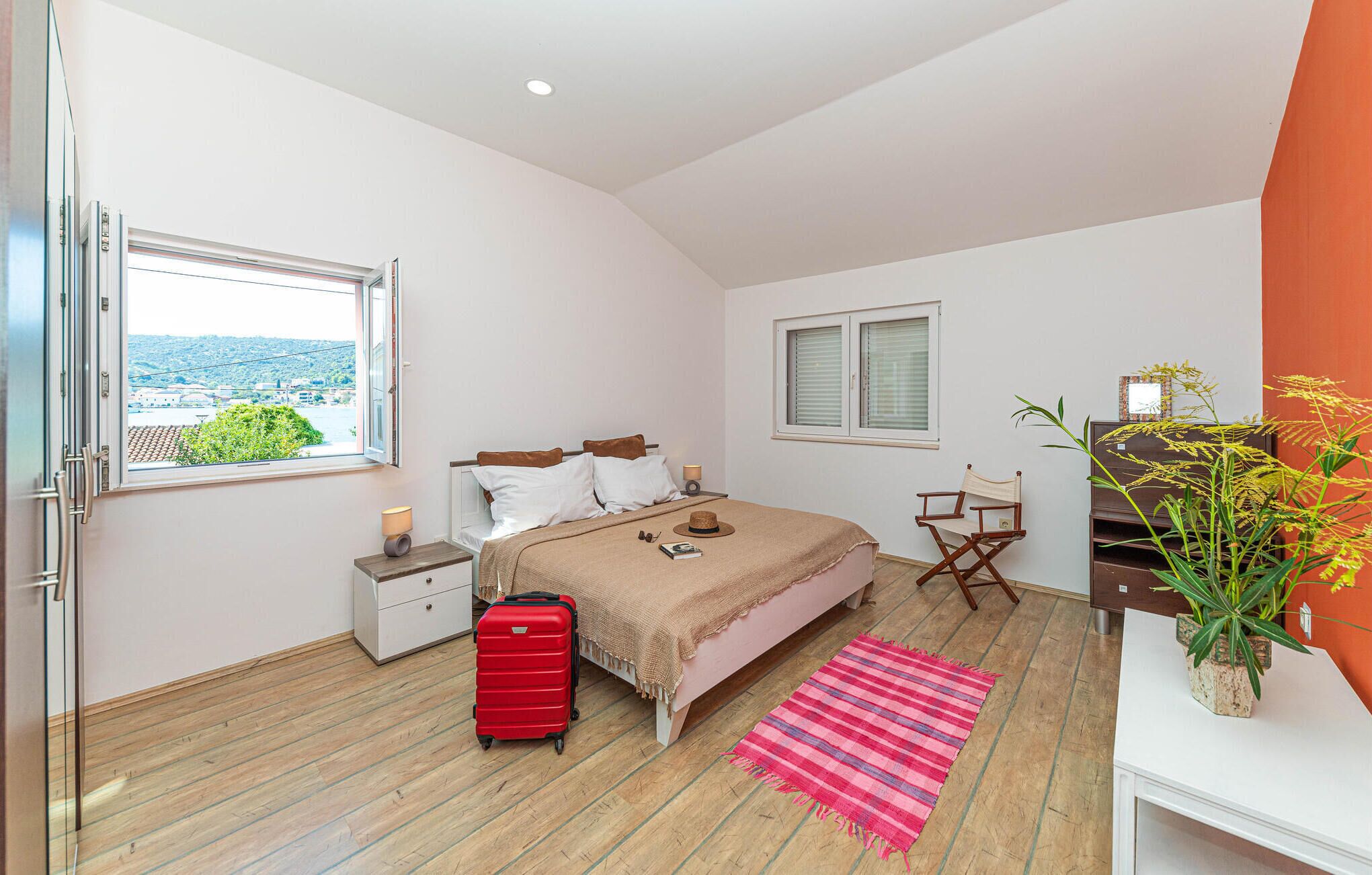 Une chambre à coucher avec un lit, une valise, un bureau avec une chaise, une fenêtre et une vue sur la verdure.