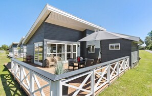 Ein modernes, zweistöckiges Haus mit einer Terrasse, großen Fenstern und einem überdachten Sitzbereich im Freien.