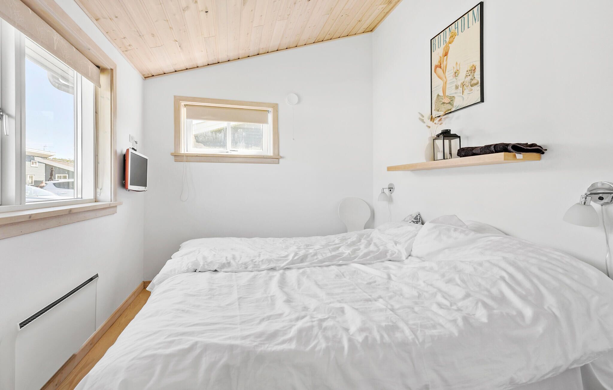 Une chambre à coucher avec un lit, une fenêtre, une petite étagère avec quelques objets et un tableau accroché au mur.