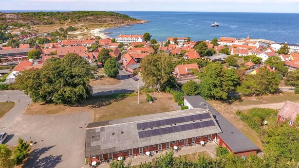 Oversigtsbillede af en kystby med røde tage, en stor bygning med solpaneler og et skib på havet.