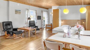 Et moderne hotelværelse med træloft, spiseplads med bord og stole, en sofa, en seng med hvidt sengetøj og et lille sofabord med en vase blomster.