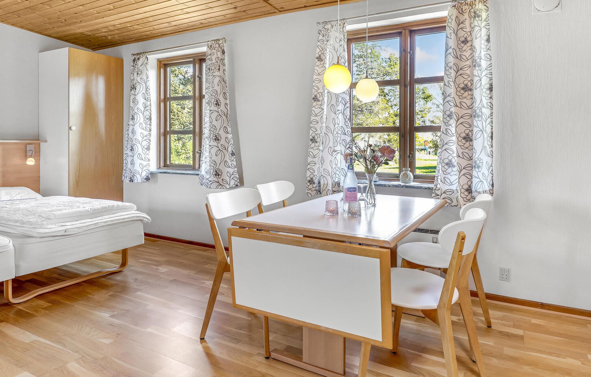 Een kamer met een bed, een eettafel met stoelen en twee ramen met bloemen gordijnen.