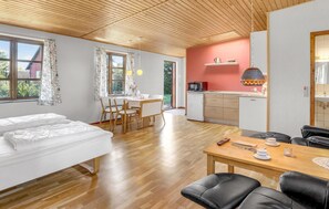 Ein modernes Zimmer mit einem Bett, einem Esstisch mit Stühlen, einer Küchenzeile inklusive Spüle und Herd sowie einem großen Fenster mit Vorhängen.