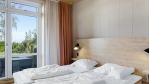 A bedroom with two beds, a wooden headboard, a nightstand with a lamp, and a view of greenery through a large window. - Awesome apartment in Allinge with WiFi (Allinge)