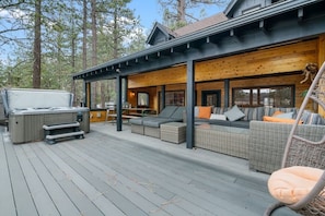 Une terrasse en bois avec des sièges d’extérieur, un jacuzzi et un espace couvert doté de grandes fenêtres.