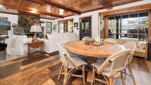 A wooden ceiling, a stone fireplace, a round dining table with wicker chairs, and a sofa. - The Black Cormorant | On the Lake (Big Bear Lake)