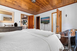 Une chambre à coucher avec un grand lit, un plafond en bois, un tableau, une télévision et une baignoire.
