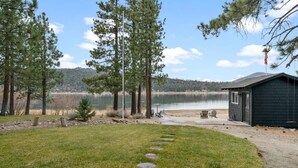 A lakeside cabin with a stone path leading to a dock, surrounded by tall pine trees and a clear view of the lake. - The Black Cormorant | On the Lake (Big Bear Lake)