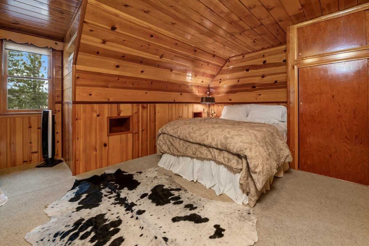A wooden cabin bedroom with a bed, a window, and a cowhide rug.