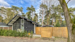 En stuga med mörkt trä på utsidan, en liten veranda och en inhägnad trädgård.