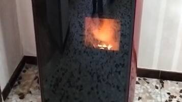 Ein schwarzer, mit Glas versehener Holzofen mit sichtbaren Flammen im Inneren, auf einem fleckigen Fliesenboden stehend.