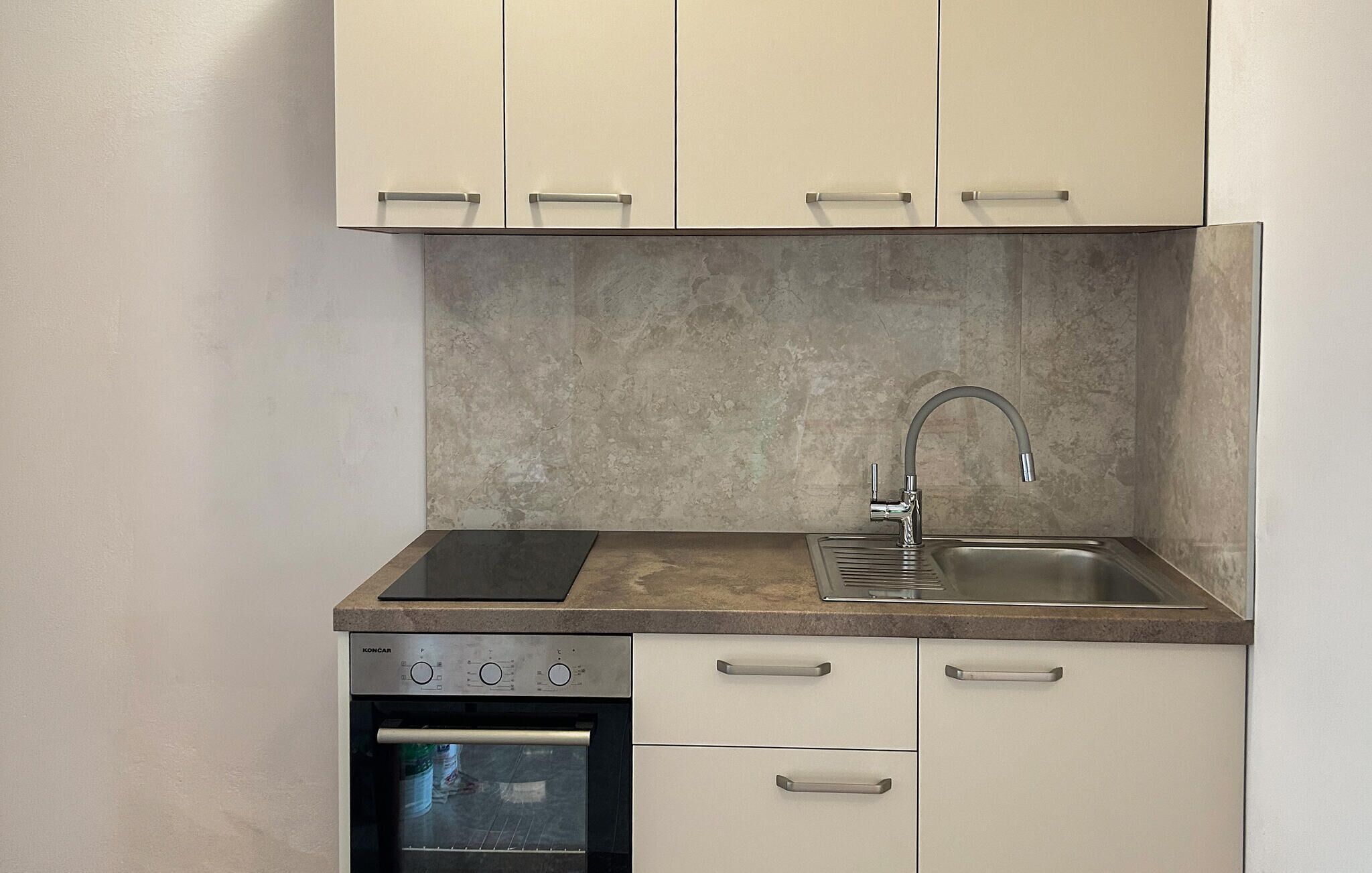 A compact kitchen with a built-in oven, a sink with a modern faucet, and a countertop with a range hood.