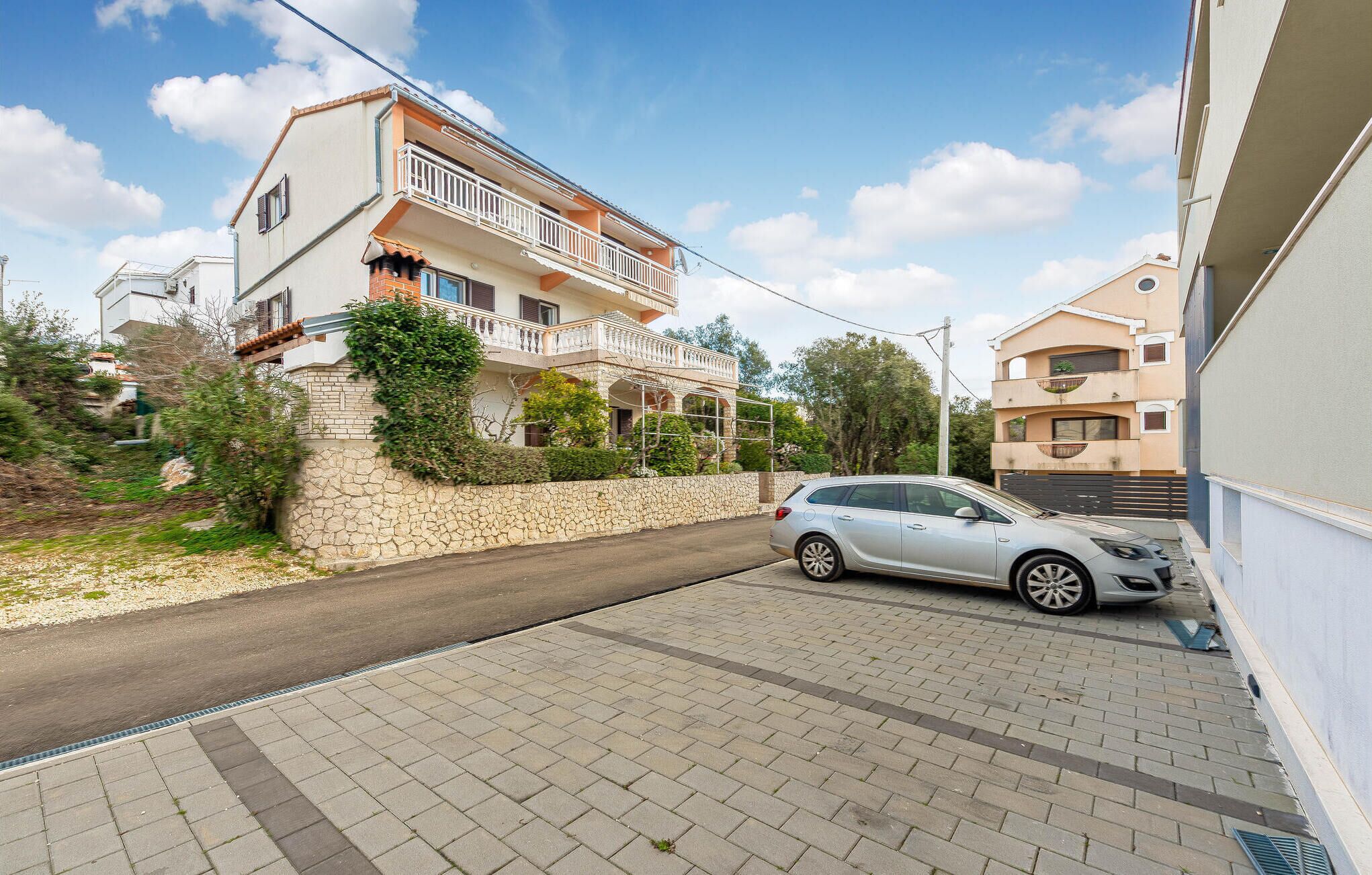 A residential street with a two-story house featuring a balcony and a parked car.