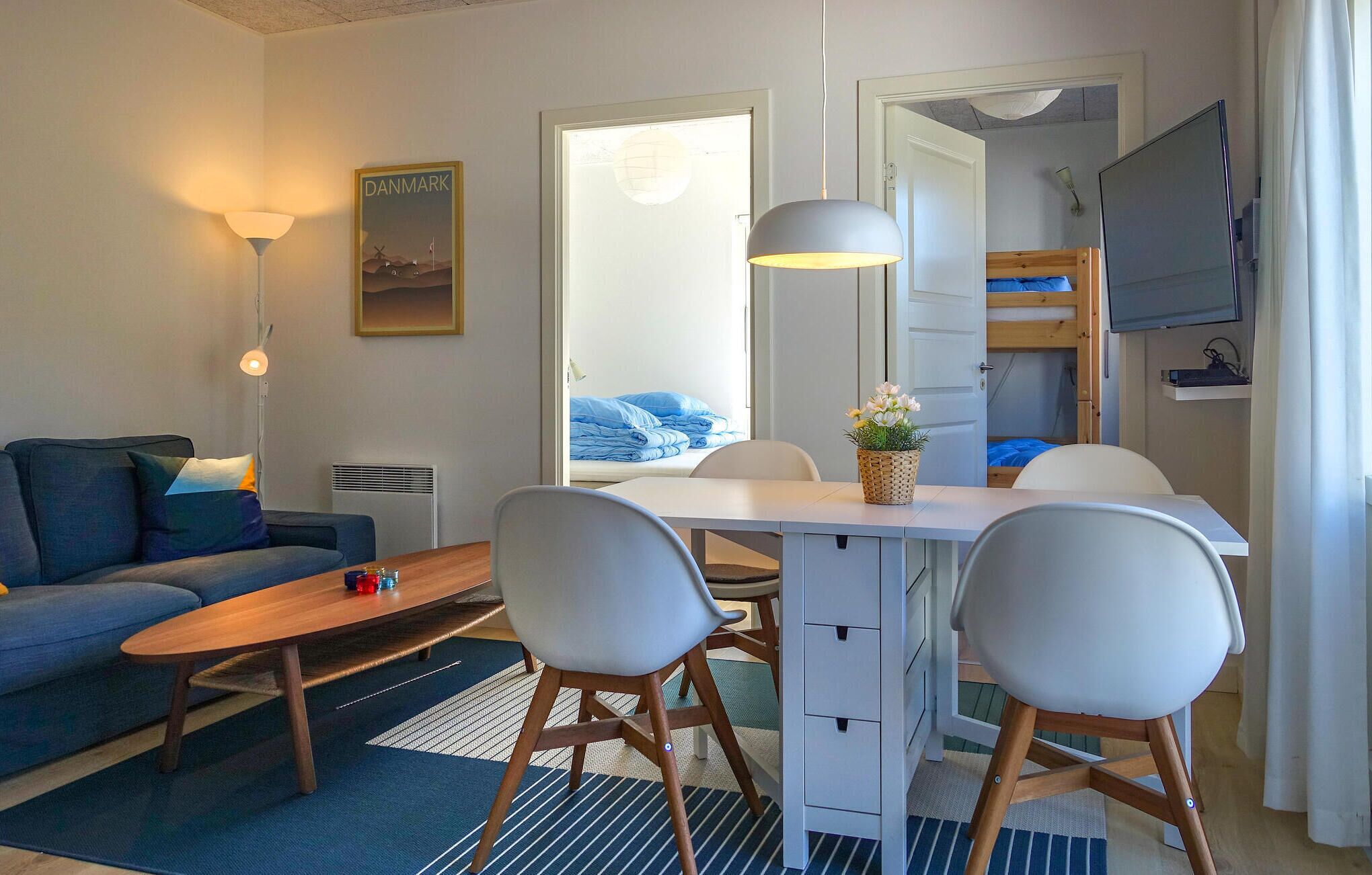 A compact hotel room with a sofa, a dining table with chairs, a small TV, and a bunk bed.