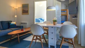 Kompakti hotellihuone, jossa on sohva, ruokapöytä tuoleineen, pieni televisio ja kerrossänky.