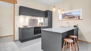 A modern kitchen with dark cabinetry, a central island, and bar stools. - 3 bedroom cozy home in Tarm (Tarm)