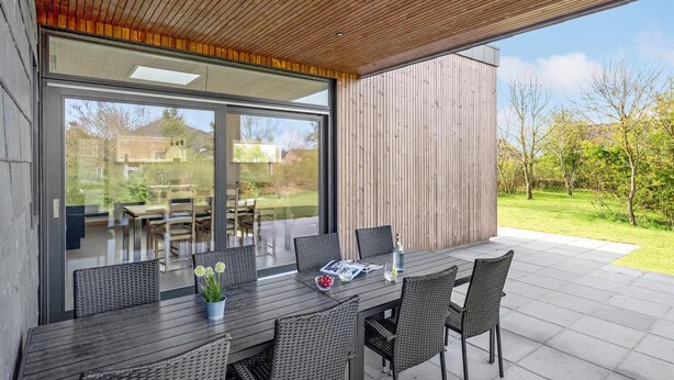 An outdoor dining area with a modern design, featuring a dark wooden table and wicker chairs. - 3 bedroom cozy home in Tarm (Tarm)