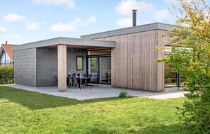 Une maison moderne dotée d’un patio comprenant une table et des chaises, une cheminée et une grande fenêtre.