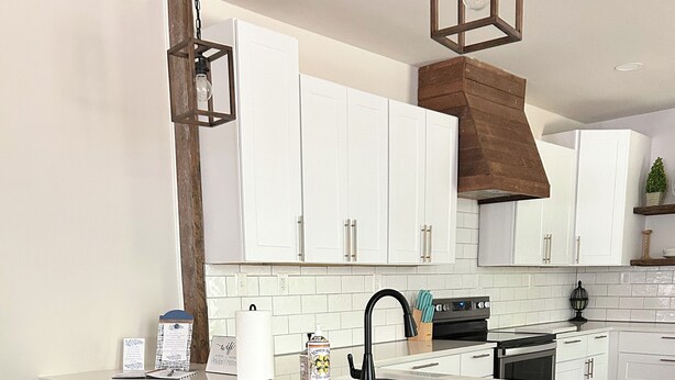 A modern kitchen with white cabinets, a large island with bar stools, a black faucet, and a wooden accent wall.