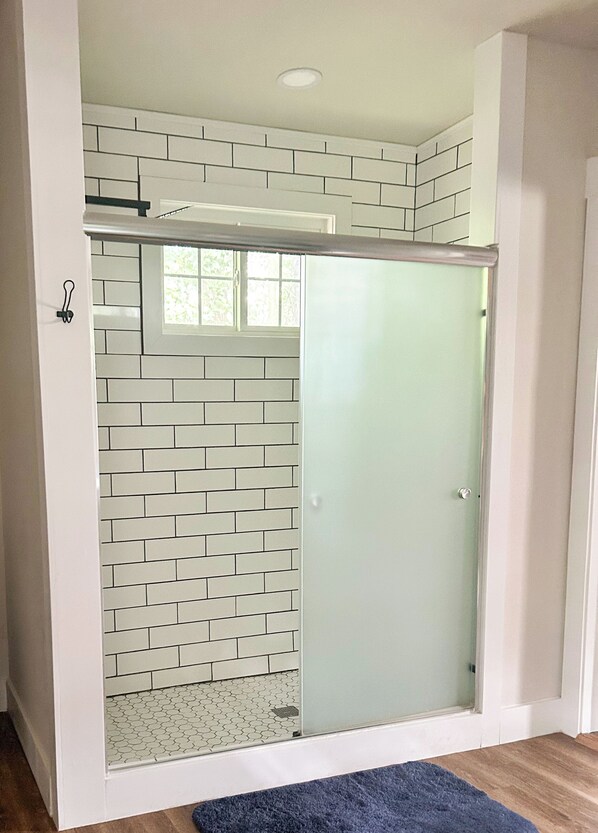 A shower with a glass door, white tiled walls, and a wooden floor.