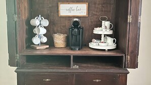 A wooden cabinet with a coffee bar sign, mugs, a coffee maker, and a tea set.