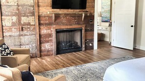 A hotel room with a wooden wall, a fireplace, a flat-screen TV, a bed, a sofa, and a door.