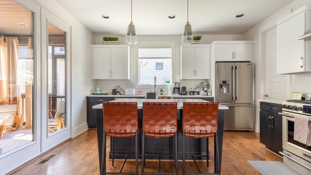A modern kitchen with a central island, bar stools, stainless steel appliances, and a view to the dining area.