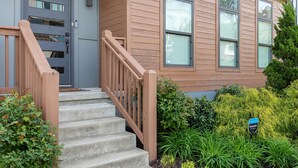 A two-story house with a wooden exterior, a front door, and a staircase leading to the entrance.