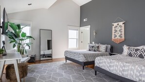 A modern bedroom with two beds, a large mirror, a potted plant, and a geometric rug.