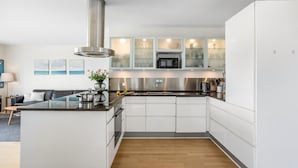 Uma cozinha moderna com armários brancos, um exaustor de aço inoxidável e uma ilha central com pia.