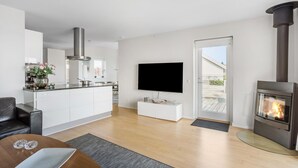 Uma sala de estar moderna com lareira, TV e área de cozinha com armários brancos e coifa de aço inoxidável.