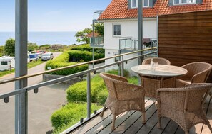 Een balkon met rieten stoelen en een tafel, met uitzicht op een weg met geparkeerde auto's en een gebouw met een rood dak.