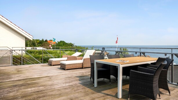 Um deck de madeira com móveis de exterior, uma mesa e vista para o mar.