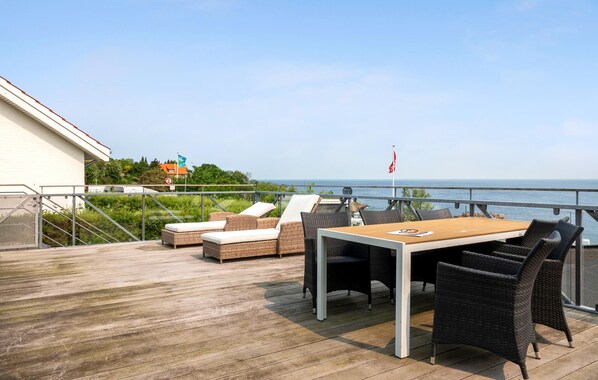 Een houten terras met buitenmeubilair, een tafel en uitzicht op zee.