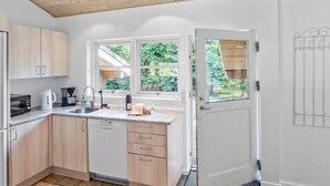 Une cuisine moderne avec des meubles en bois, un lave-vaisselle, un évier et une fenêtre donnant sur un espace verdoyant.