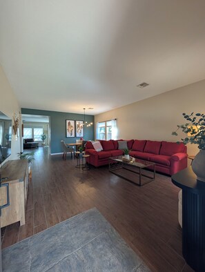 Ein geräumiges Wohnzimmer mit einem roten Sofa, einem Couchtisch und einem Essbereich im Hintergrund.