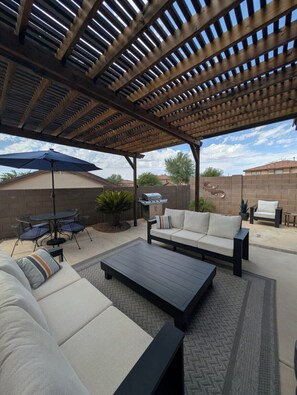 An outdoor patio with a pergola, a barbecue grill, a sofa, and a dining table.