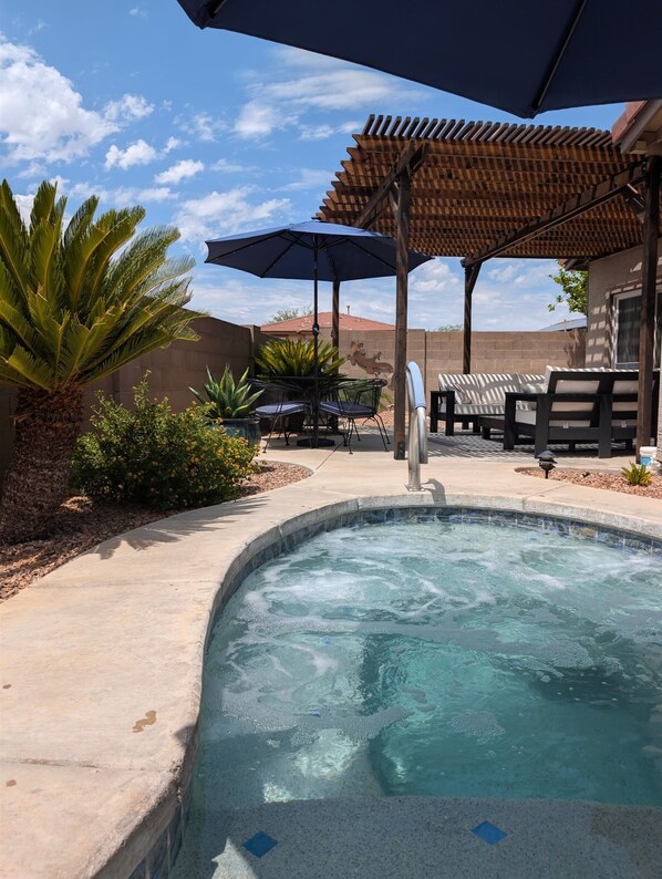 A swimming pool with a wooden pergola overhead, surrounded by lounge chairs and a palm tree.