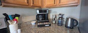 A kitchen with a coffee maker, grinder, kettle, and utensils.