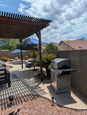 Un patio al aire libre con una parrilla, una zona de estar cubierta y una piscina.