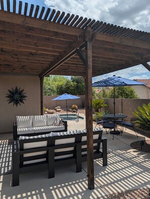 A covered patio area with a pool, outdoor furniture, and a decorative sun on the wall.