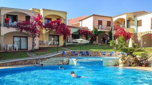 A swimming pool with two people swimming, surrounded by buildings with balconies and red flowering plants. - Cozy apartment in Badesi (Badesi)