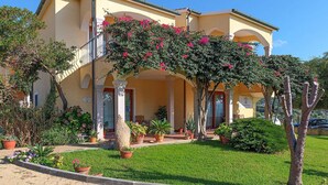 A two-story building with a covered porch, columns, and potted plants. - Cozy apartment in Badesi (Badesi)