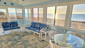 A sunroom with a view of the beach, featuring a white wicker sofa, a glass table, and a patterned rug. - Great price!Beachfront with Stunning gulf view from this Great home with hot tub (Saint George Island)