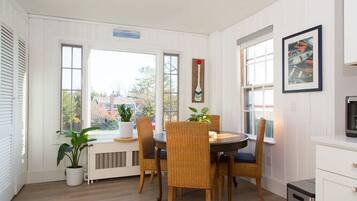 A dining area with a round table, wicker chairs, potted plants, and a view of the outside.